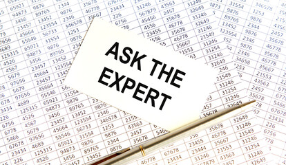 Obraz premium On the white business card the inscription ASK THE EXPERT, next to the pen and all on the background of accounting. Business concept