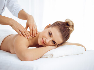 Obraz na płótnie Canvas Young and blonde woman enjoying massage of back in spa salon. Beauty concept