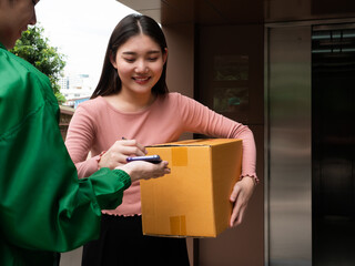 Asian young girl holding parcel and writing signature online in application via smartphone with...