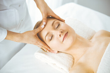 Beautiful happy woman enjoying facial massage with closed eyes in spa salon. Relaxing treatment in medicine and Beauty concept