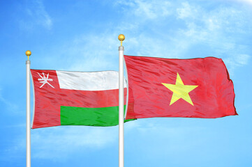 Oman and Vietnam two flags on flagpoles and blue sky