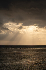 The sun's rays over the sea, burst out of the cloud. Dramatic sunset on the sea, beautiful peaceful scene, rays of light shine in water, sunbeam in cloudy sky, summer ocean view, with fisherman