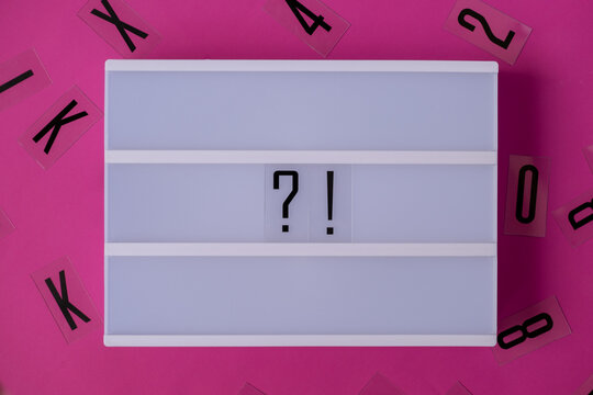 Lightbox mit einem Fragezeichen und Rufzeichen "?!" auf einem pinken Hintergrund mit Buchstaben