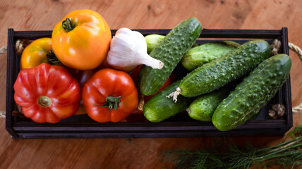 Vegetables tomatoes and cucumbers in a wooden box on a wooden table, close-up. Harvest, garden, vegetable garden. Blurred bokeh background.