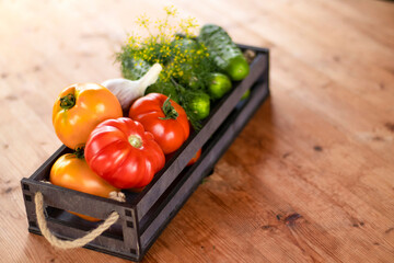 Vegetables tomatoes and cucumbers in a wooden box on a wooden table, close-up. Harvest, garden, vegetable garden. Blurred bokeh background.