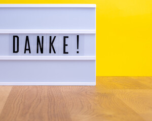 Lightbox mit dem Wort "Danke!" auf einem hellen Holztisch vor einem gelben Hintergrund