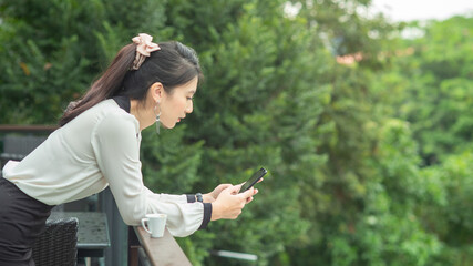 Young business women stand on the balcony and are using mobile phones.