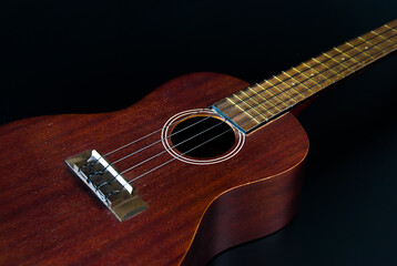 Brown wood ukulele in a black background shot at the side corner.