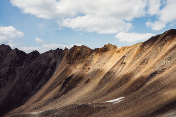 Fototapeta premium Atmospheric landscape with rocky mountain wall with pointy top in sunny gold light. Beautiful golden rock pinnacle in sunlight. Awesome mountain scenery with pointed rockies. Sharp stony mountains.