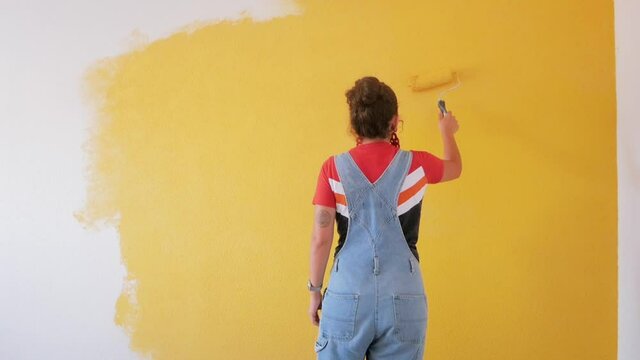Woman painting a room with yellow color using a paint roller. Alone woman painting house