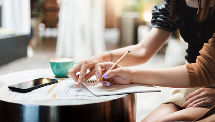 Two young asian woman working together and writing plan in book
