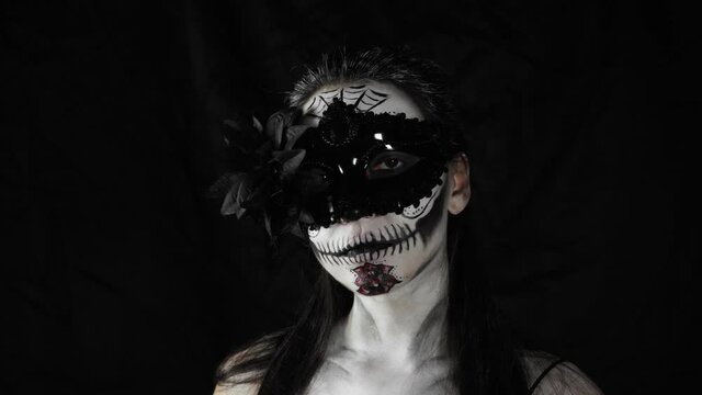 Mexican day of the dead. Young woman with sugar skull Halloween makeup looks at the camera. The woman removes the mask from her face. Happy Halloween. High quality 4k video