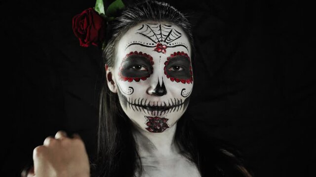 Mexican day of the dead. Young woman with a sugar skull Halloween makeup turns and looks at the camera. Happy Halloween. High quality 4k footage