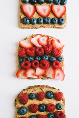 Three peanut butter toasts with fresh berries. Whole meal brown bread with creamy spread, blueberry, raspberry and strawberry topping