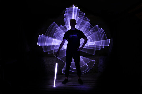 Silhouette of a man standing with a lightsaber with neon drawings and leds at lightpainting. Inscription "escape" on t-shirt.