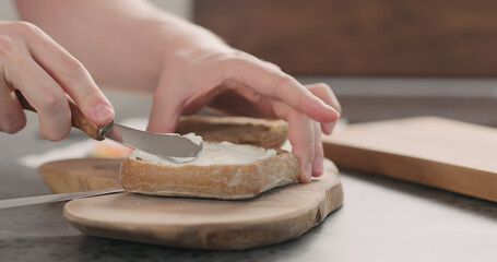 man hands spreading cream cheese over ciabatta to make sandwich on wood board