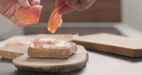 man hands put smoked salmon on ciabatta with cream cheese to make a sandwich on wood board