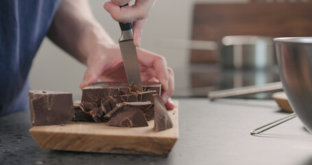 man hands breaking big dark chocolate block with knife on wood board