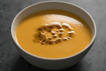 Pumpkin soup decorated with herbs and olive oil in white bowl on concrete background