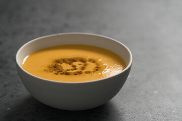 Pumpkin soup decorated with herbs and olive oil in white bowl on concrete background with copy space