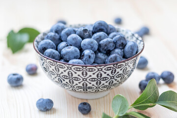Fresh organic blueberries in small bowl on natural wooden background.