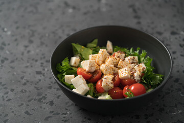 Healthy light salad with cherry tomatoes, mozzarella and frisee in black bowl on concrete surface