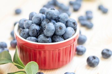 Fresh organic blueberries in red bowl on natural wooden background.