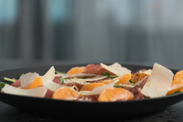 Salad with prosciutto, tangerines and vintage cheese on black plate