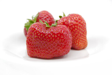 Three red ripe strawberries on a white plate. Strawberries isolated on a white background.