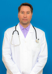 Fototapeta premium vertical photo A male doctor with a stethoscope smiling a clipboard while standing in a clinic. on light blue background