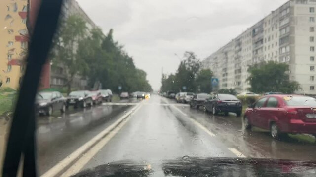 Drive a car on a cloudy rainy day. Splashes from a puddle on the road flood the windshield. View from the driver's seat.