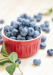 Fresh ripe organic blueberries in red bowl on natural wooden background.