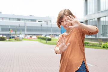 Adult redhead woman in casual clothes holding out her hand with open palm and showing stop gesture....