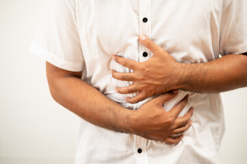 A man in white shirt with a stomach ache He squeezed his stomach with both hands. Because he ate bad and poisonous food he has go to toilet now.
