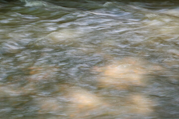 Blurred background with the surface of a fast flowing mountain river. A shallow clear mountain stream through which the stones at the bottom are visible.