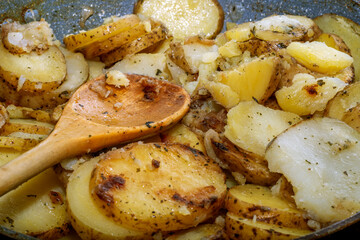 Hot baked potato slices with thin-skinned potatoes with a wooden spoon. A simple and quick after-work meal for the worker and bachelor