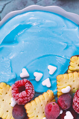 Detail shot of healthy fruit smoothie bowl dyed blue with natural spirulina powder and topped with red raspberry and cranbery and small biscuits