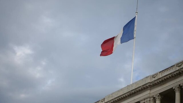 France flag waving in the wind on top of administrative building against the dark rainy sky. France travel concept