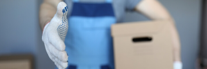 Loader man with box stands holding out his hand. Company takes all stages furniture transportation on itself. Arrange office relocation. Throw away unnecessary trash. Office furniture packaging