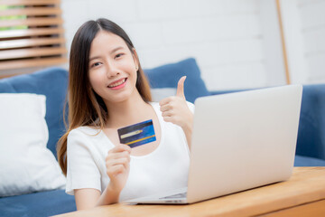 Young asian woman sit on sofa using laptop computer shopping online with credit card buying to internet, happy girl payment with e-business on couch, purchase and payment, business concept.