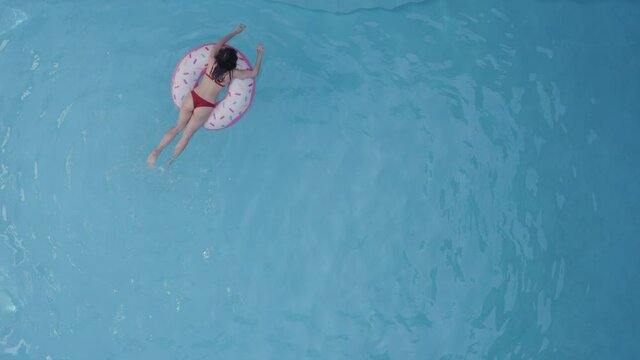 Alone young woman student daughter chilling relaxing swimming floating in inflatable tube circle round pink donut in blue pool on summer holiday resort party celebration abroad, full-length shooting