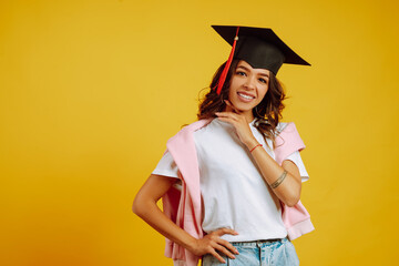 Portrait of African American girl in a graduation hat on her head posing on a yellow background. Graduation, university, college, distance education concept.