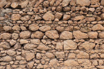 old stone wall is constructed of yellow rough stones of different sizes. seamless texture.