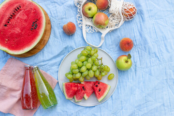 Summer picnic setting with a variety of delicious fruits, watermelon and refreshing drinks on a blue blanket. Beautiful lifestyle concept. Top view. copy space.