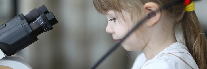 Little girl on field trip looks through microscope. Child has fun at workplace parents during...