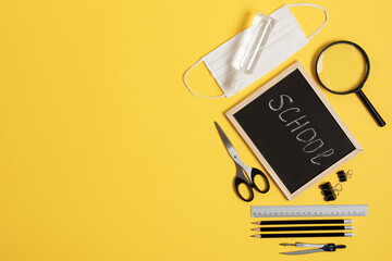 Blackboard with school and office supplies on yellow background top view during coronavirus time.