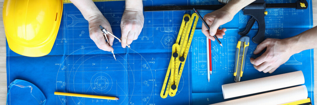 Top view of two architects painting project of house. Professional master-builder using pencil and compass for drawing. Architecture and construction concept