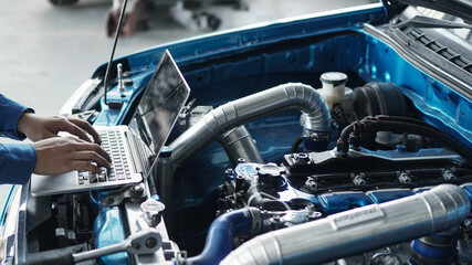 Mechanic using laptop computer working tuning on car for the efficiency of the race car in garage.maintenance concept