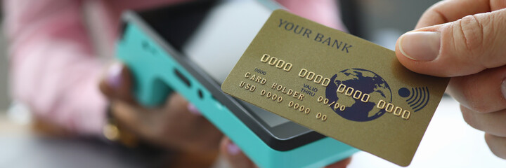 Close-up of hand holding gold credit card. Person paying for service or product. Female worker giving terminal for repayment. Banking and outpayment concept