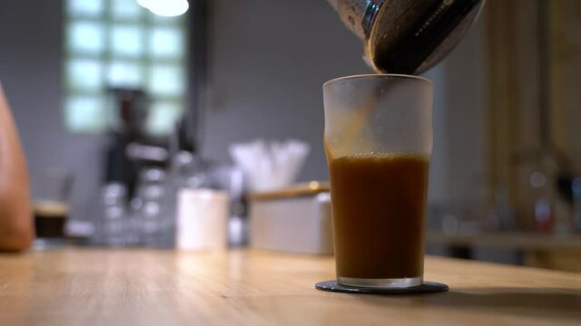 Hand pouring nitro cold brew coffee from the maker into glasses cup